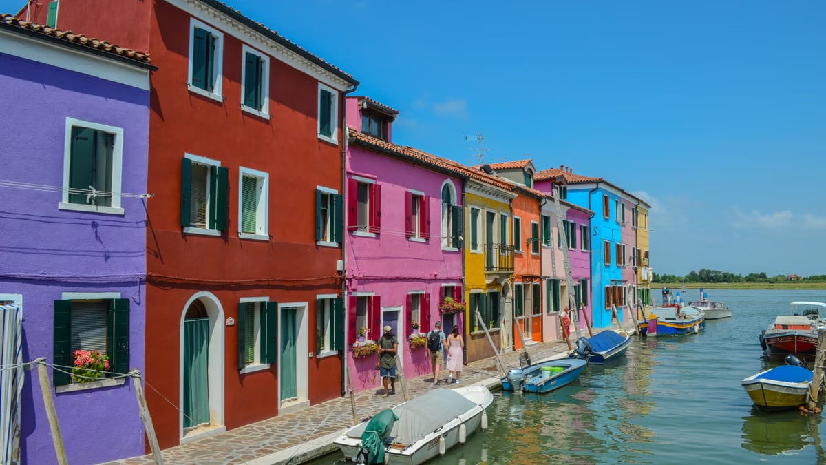 Vibrant multi-colored houses line a canal in Burano, Venice, Italy, capturing its iconic architecture.